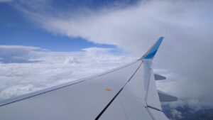 View outside an airplane window, including wing and soft clouds in the daylight