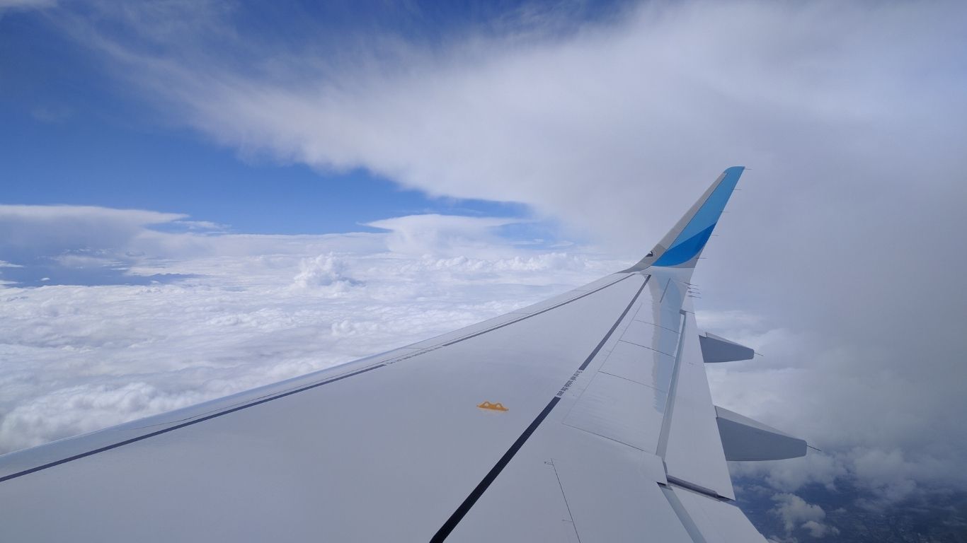 View outside an airplane window, including wing and soft clouds in the daylight